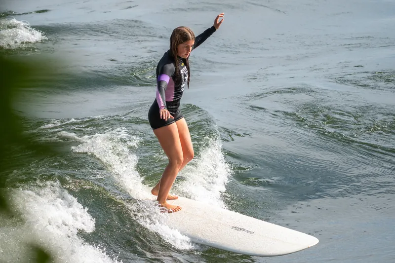 Une surfeuse, un bras levé, glisse sur un longboard blanc