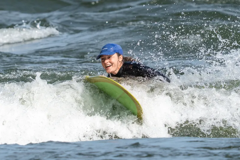 Une surfeuse en casquette bleue, tout sourire, émerge de l'écume
