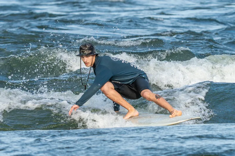 Un surfeur accroupi, les bras tendus, dans l'écume de la vague