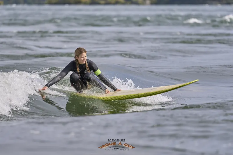Une surfeuse accroupie, main sur la planche, dans l'écume