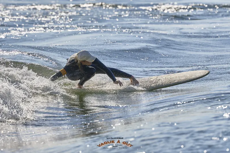 Une surfeuse penchée en avant, main dans l'eau, sur un longboard