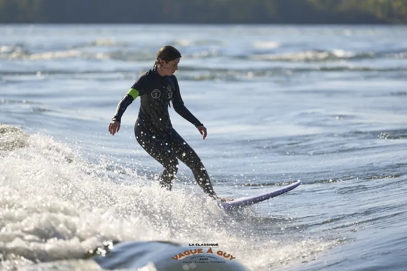Une surfeuse glisse sur la vague, bras tendus, dans l'écume