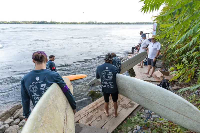 Des surfeurs, planche sous le bras, descendent vers la rivière